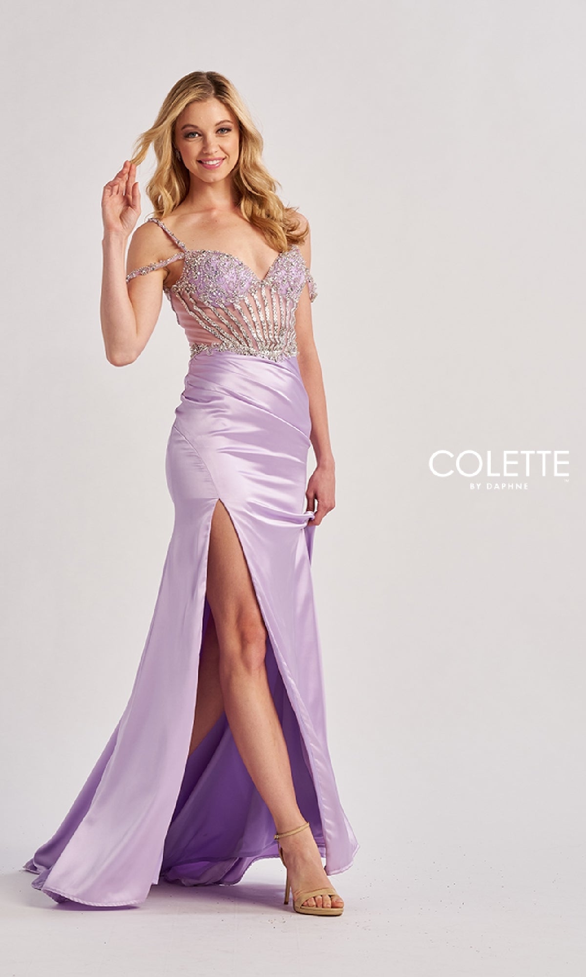 A woman in the Colette CL8460 long prom dress with a light purple off-the-shoulder beaded bodice, thigh-high slit, and lace-up open back stands smiling against a plain background. The Colette by Daphne logo is visible.
